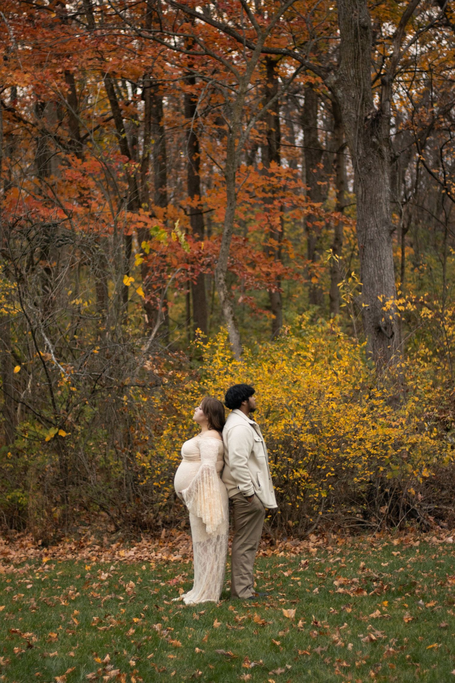 Couple standing in autumn forest surrounded by golden leaves and fall colors.