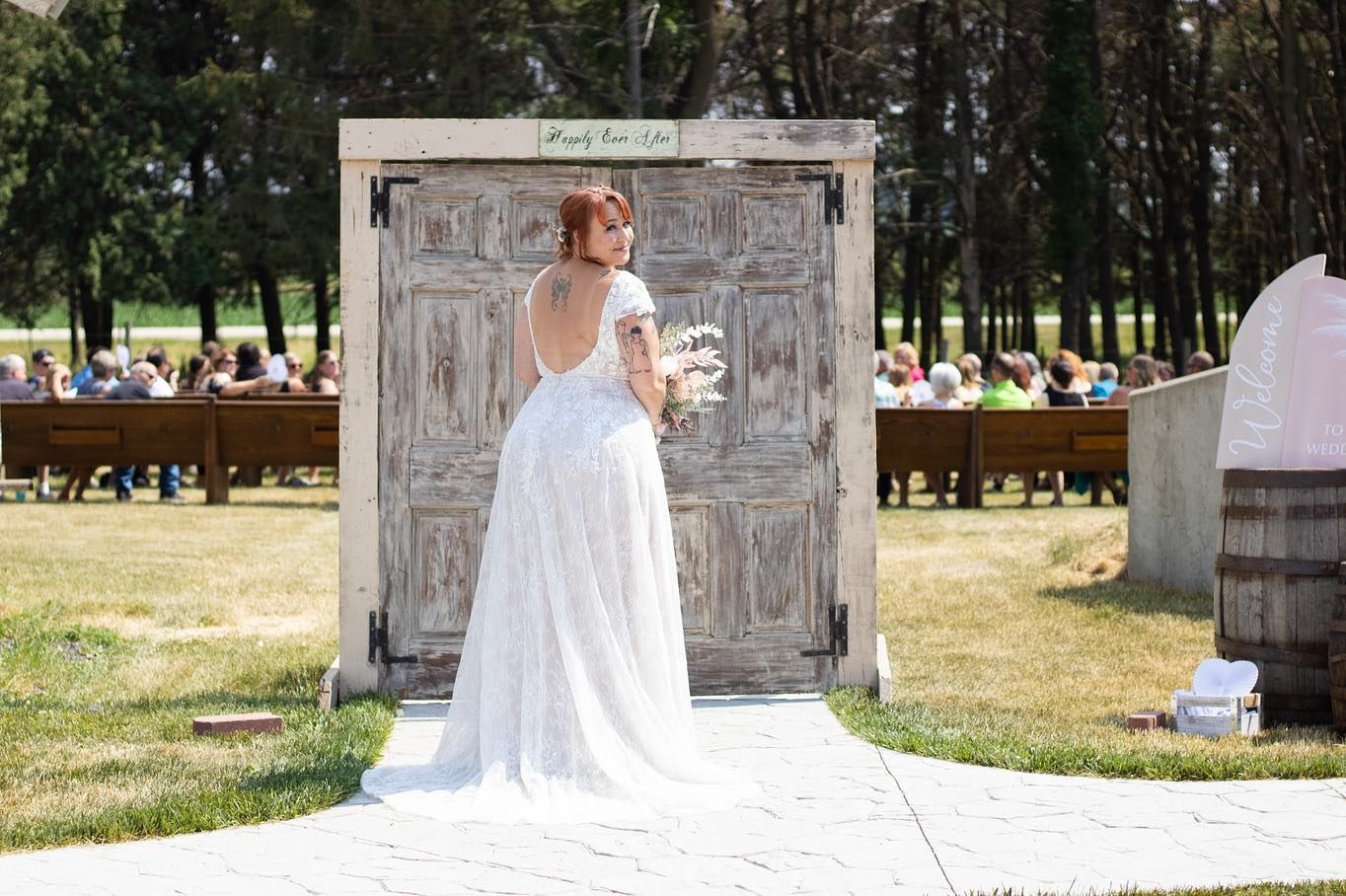 A bride in a flowing white gown stands in front of vintage doors at an outdoor wedding venue.