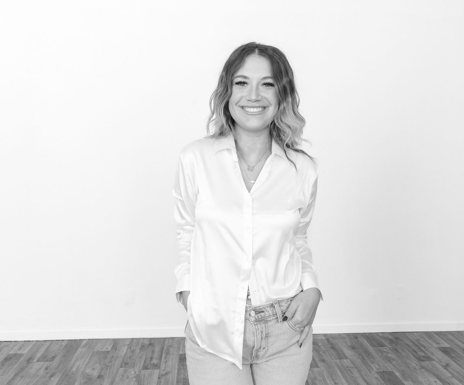 A casual portrait against a white background featuring a white button-down shirt and light denim.