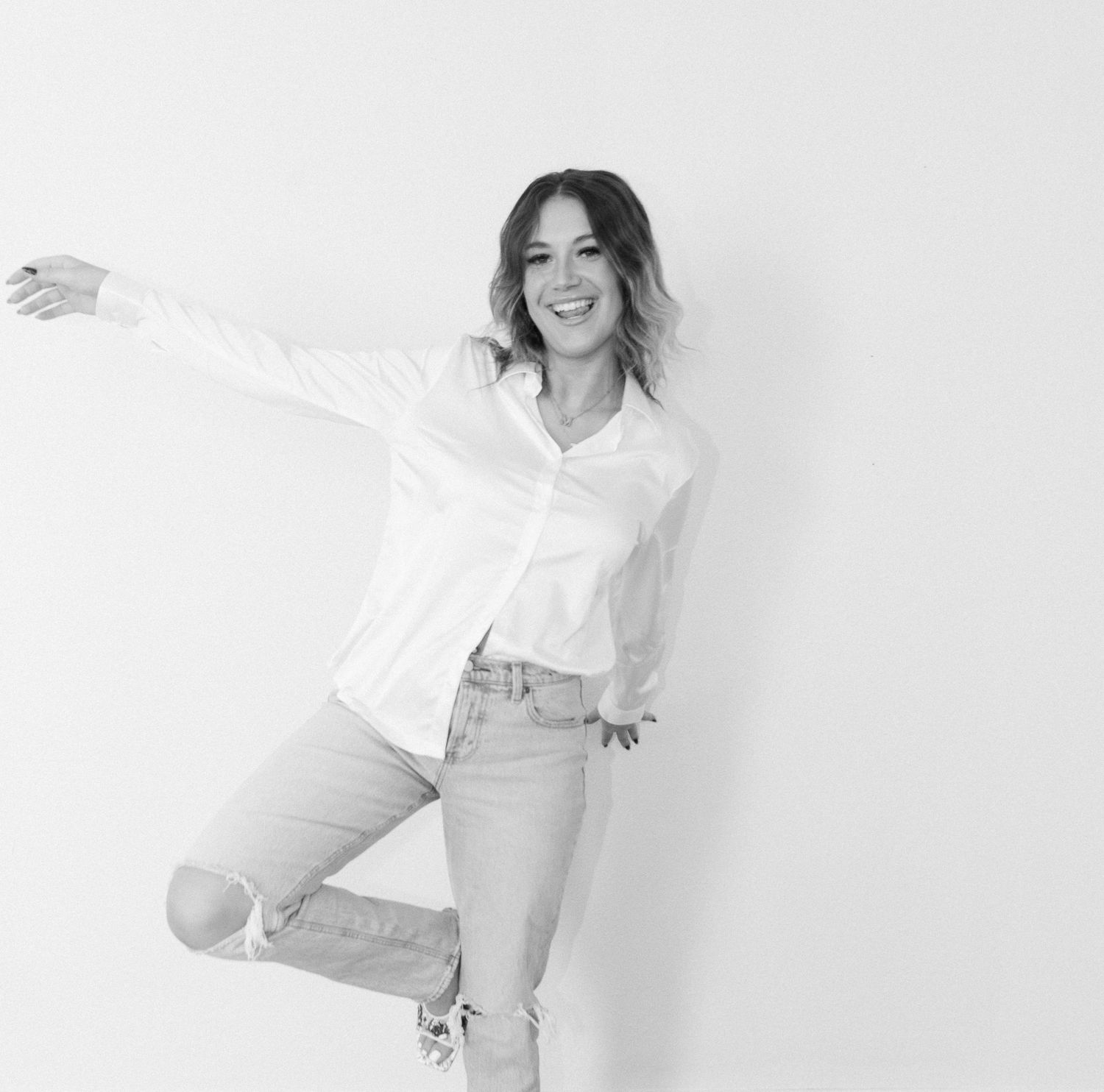 A casual fashion pose in a white button down shirt and distressed jeans against a white background.