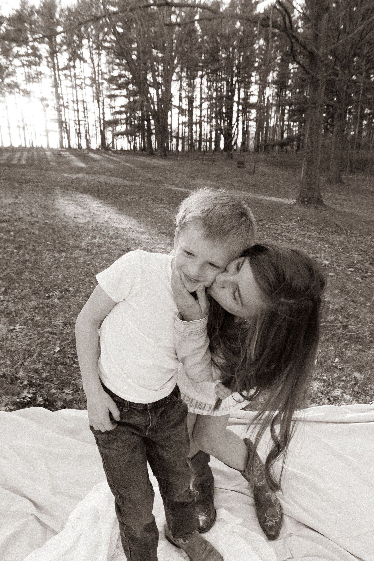 A joyful candid moment captured on a blanket in a wooded setting with pine trees in the background.