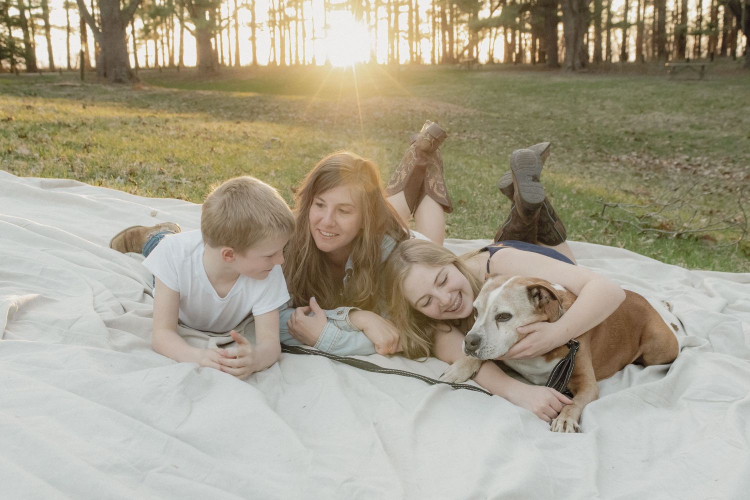 A relaxed outdoor scene with children and a dog lying on a blanket at sunset in a grassy field.