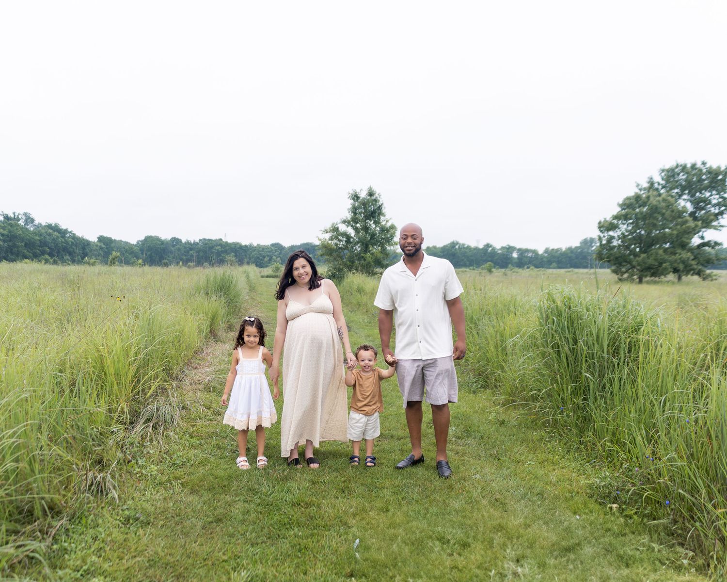 A family walks together on a winding path through tall green grass during a summer afternoon.