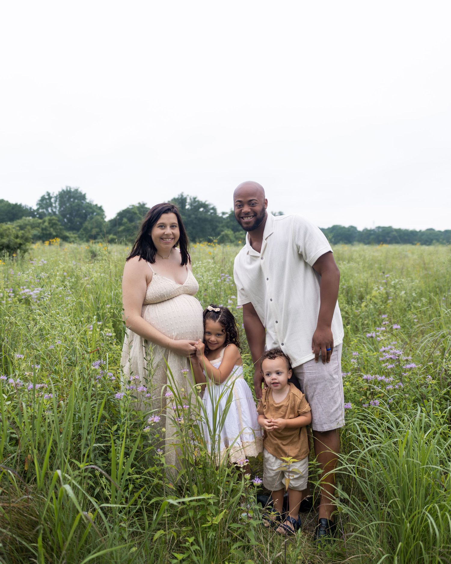A family stands together in a tall grassy meadow filled with wildflowers on a summer day.