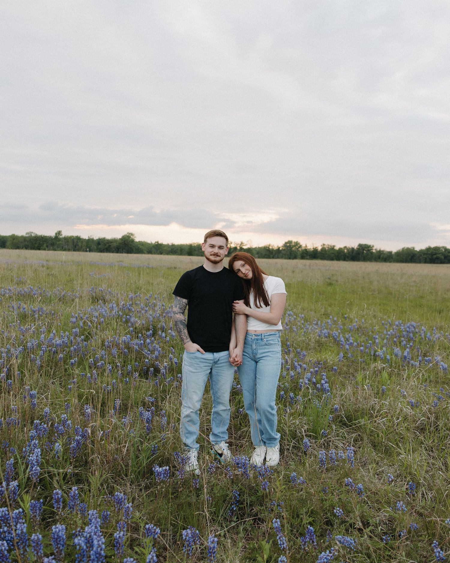 A couple stands together in a field of vibrant bluebonnets during sunset in Texas.
