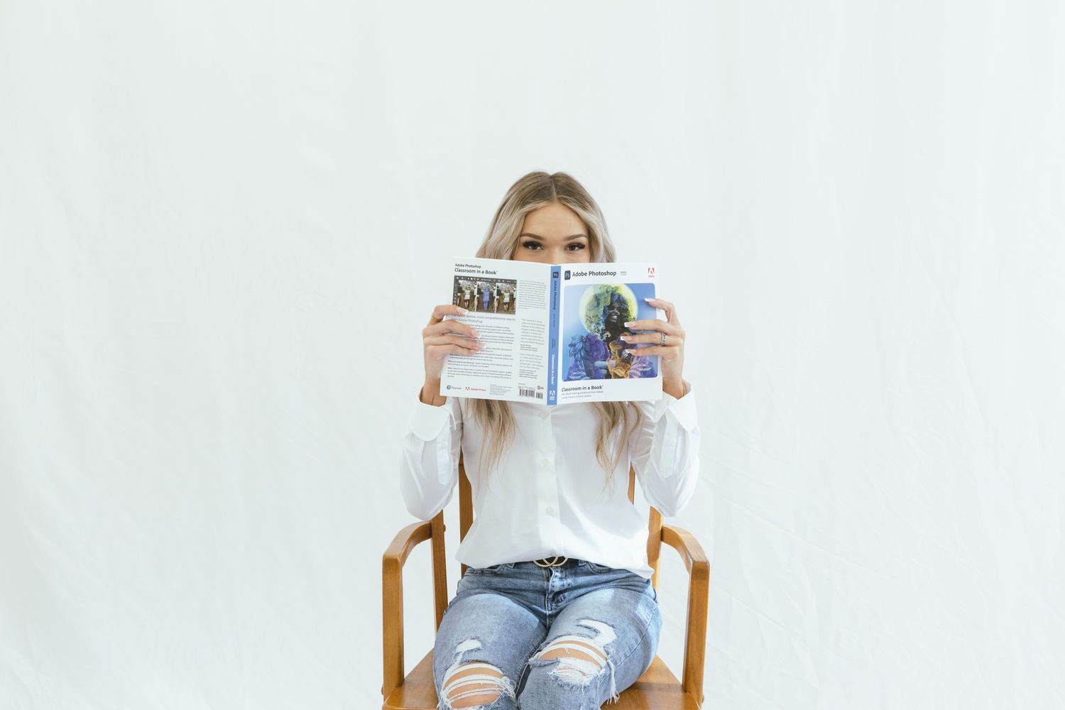 Person sitting in wooden chair reading newspaper against white background.