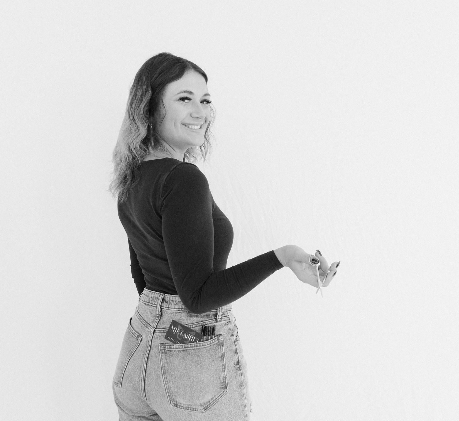 Woman in black top and jeans poses against white background.