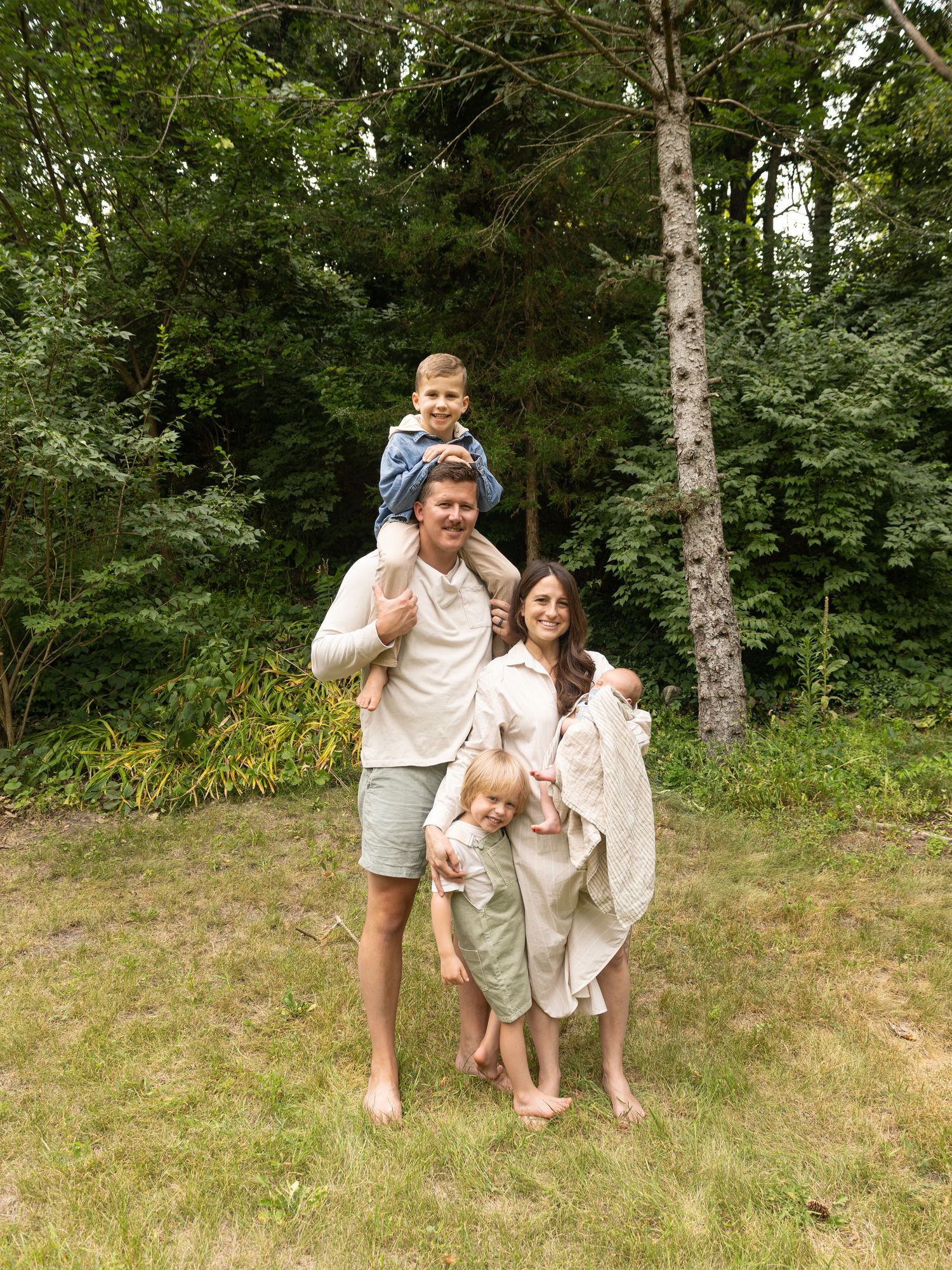 A family enjoys a summer day outdoors together in a wooded area with lush green trees in the background.