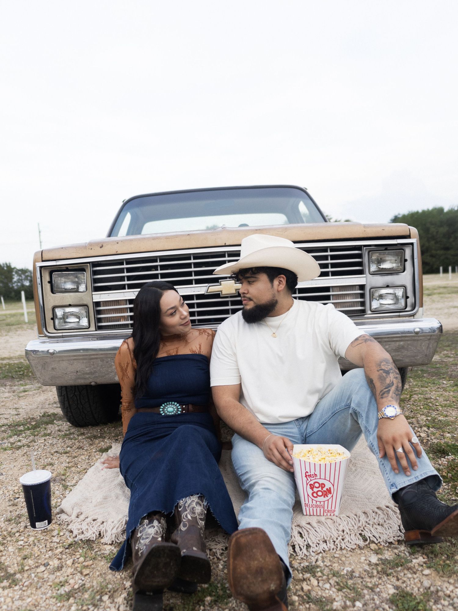 A couple shares an intimate moment while sitting on rocks against a vintage Ford truck in a rustic outdoor setting.