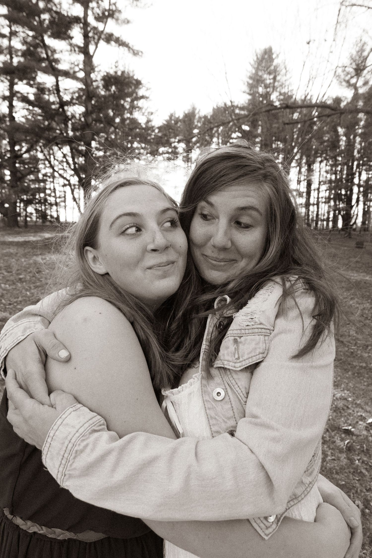 Two friends sharing a warm embrace and smiling in a natural outdoor setting with trees behind them.