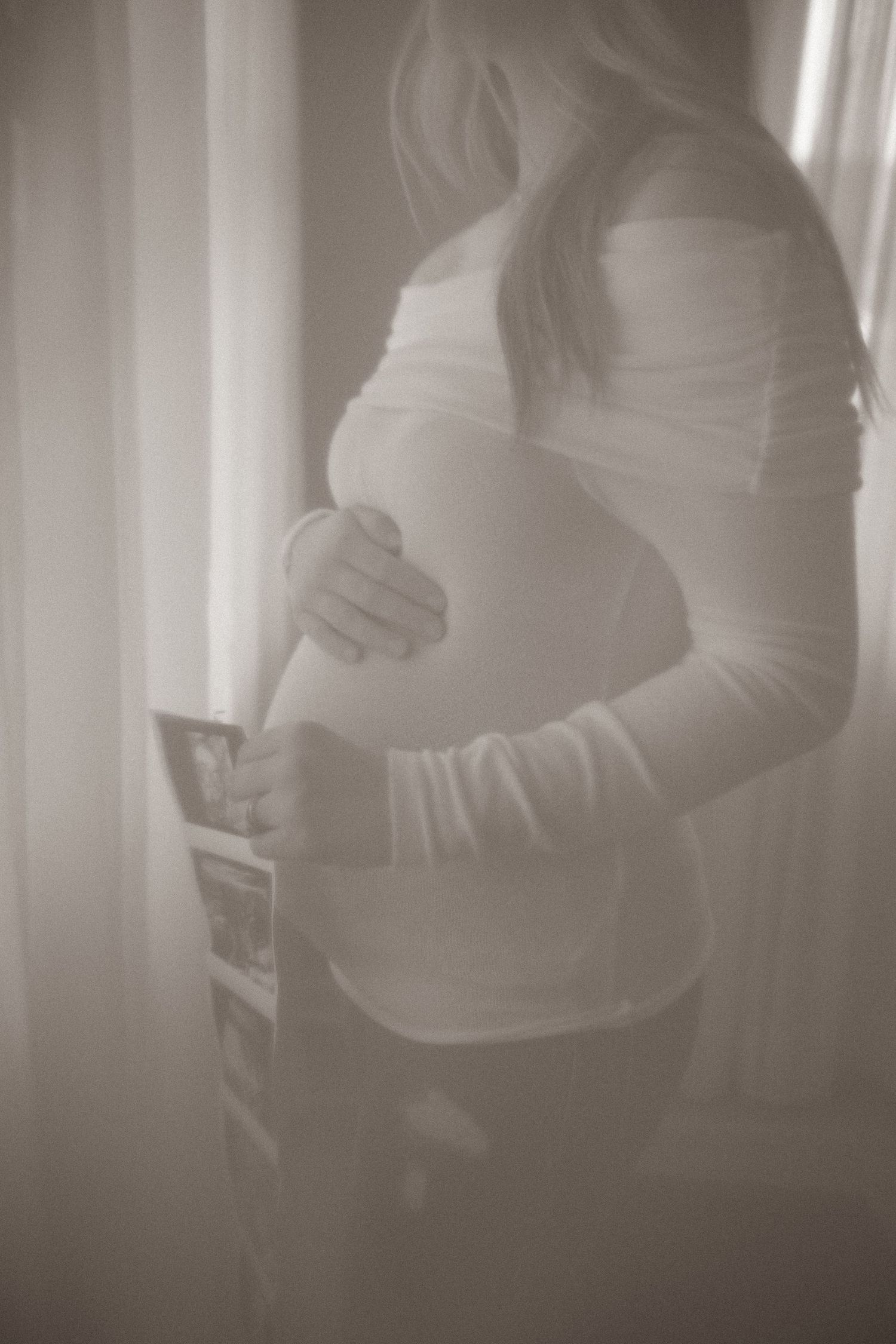 A soft, dreamy maternity photo showing a growing baby bump in natural window light.