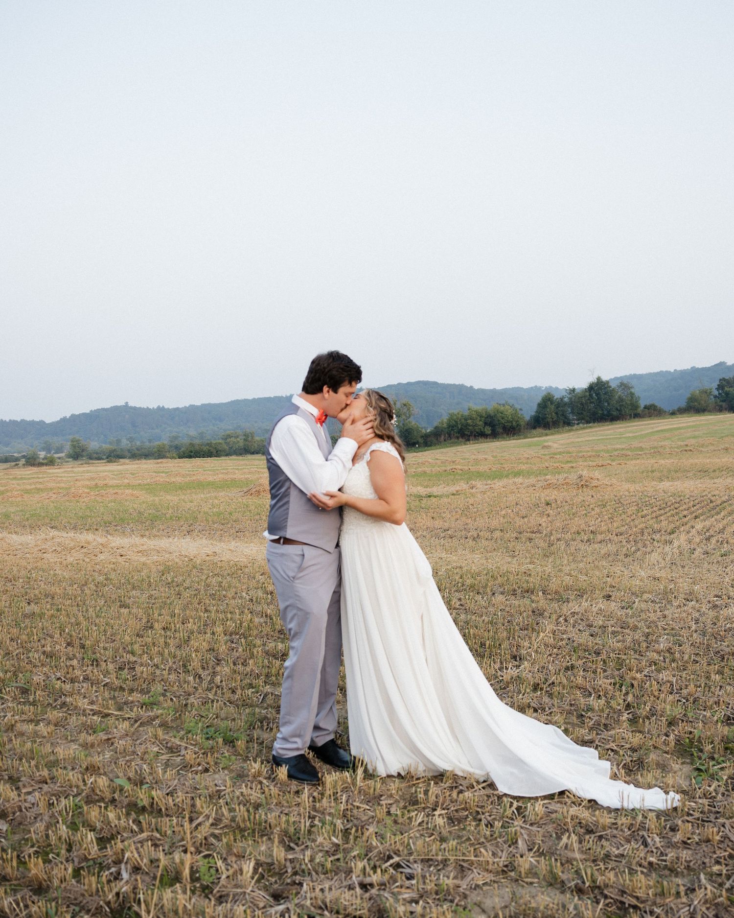 A romantic wedding couple shares a tender moment in a golden field with rolling hills in the background.