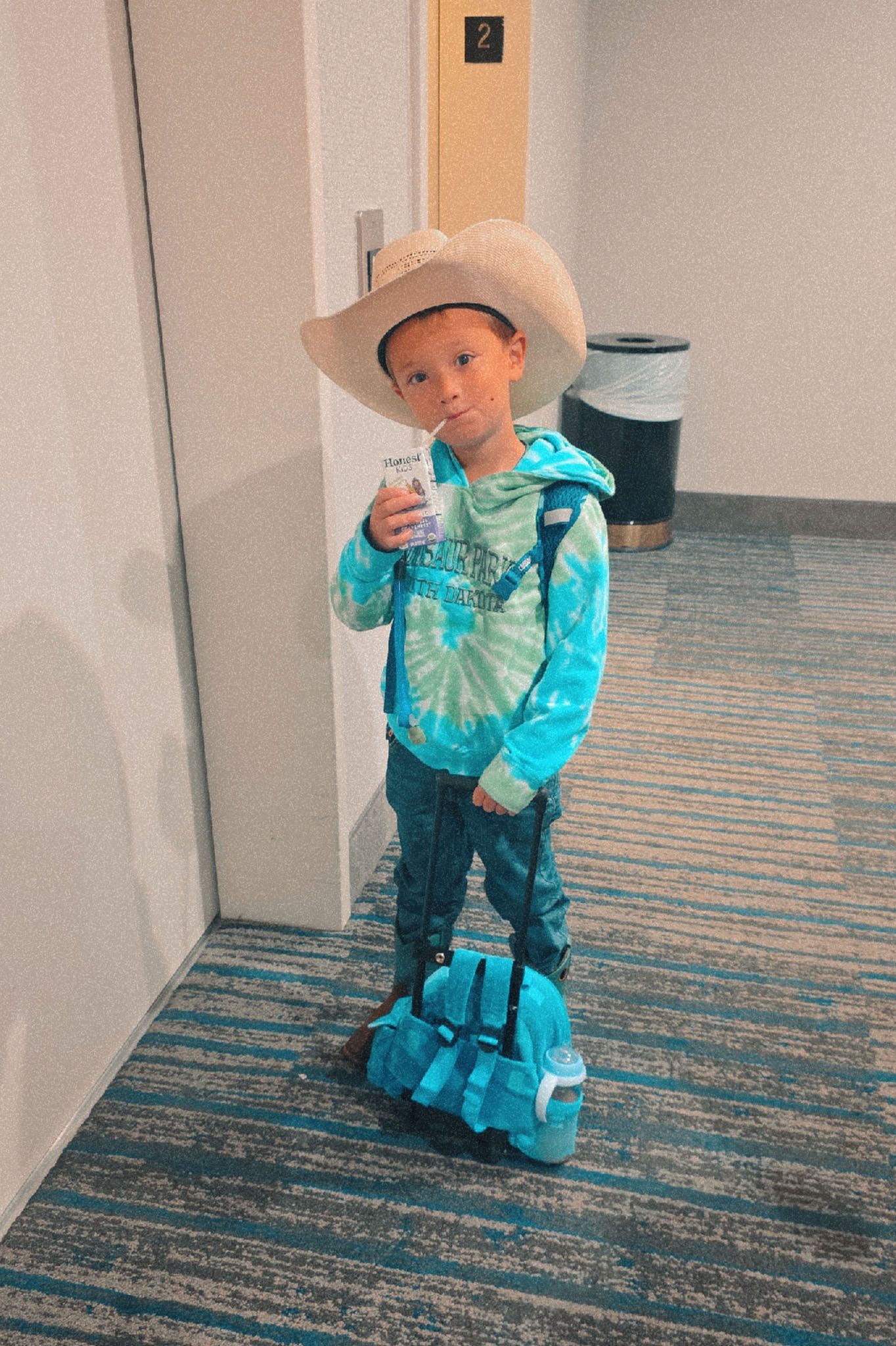 Young boy in cowboy hat and tie-dye hoodie leaving Hampton Inn, Scottsbluff