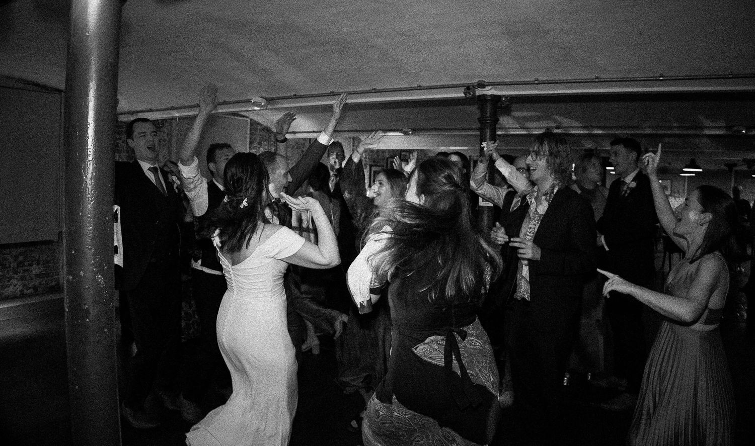 Black and white photo of wedding guests dancing energetically at a lively wedding reception party.