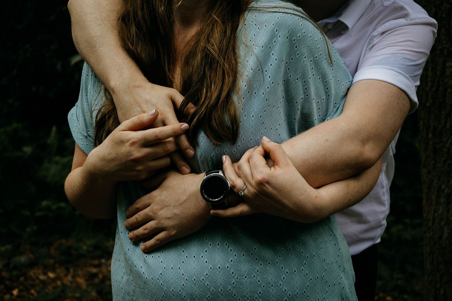 Two people sharing a warm embrace outdoors in a forest setting, with one wearing a watch.