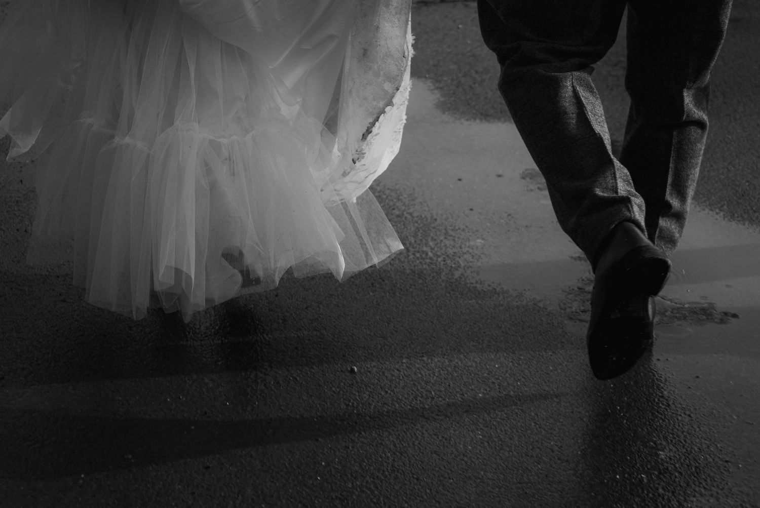 Black and white photo of a bride and groom running in the rain, showing their feet and lower bodies.