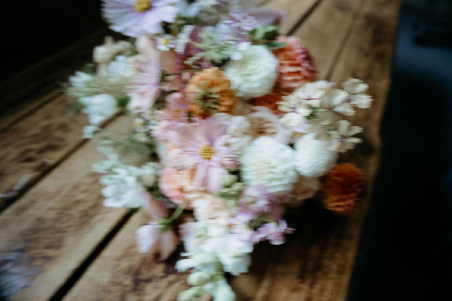 Soft blurry bridal bouquet with white, pink, and peach flowers arranged on a rustic wooden surface.