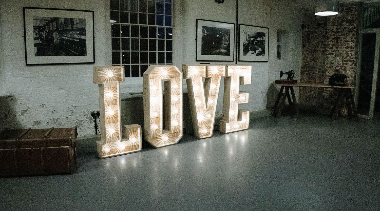 Large illuminated LOVE letters with vintage bulbs displayed in a rustic industrial venue with concrete floors.