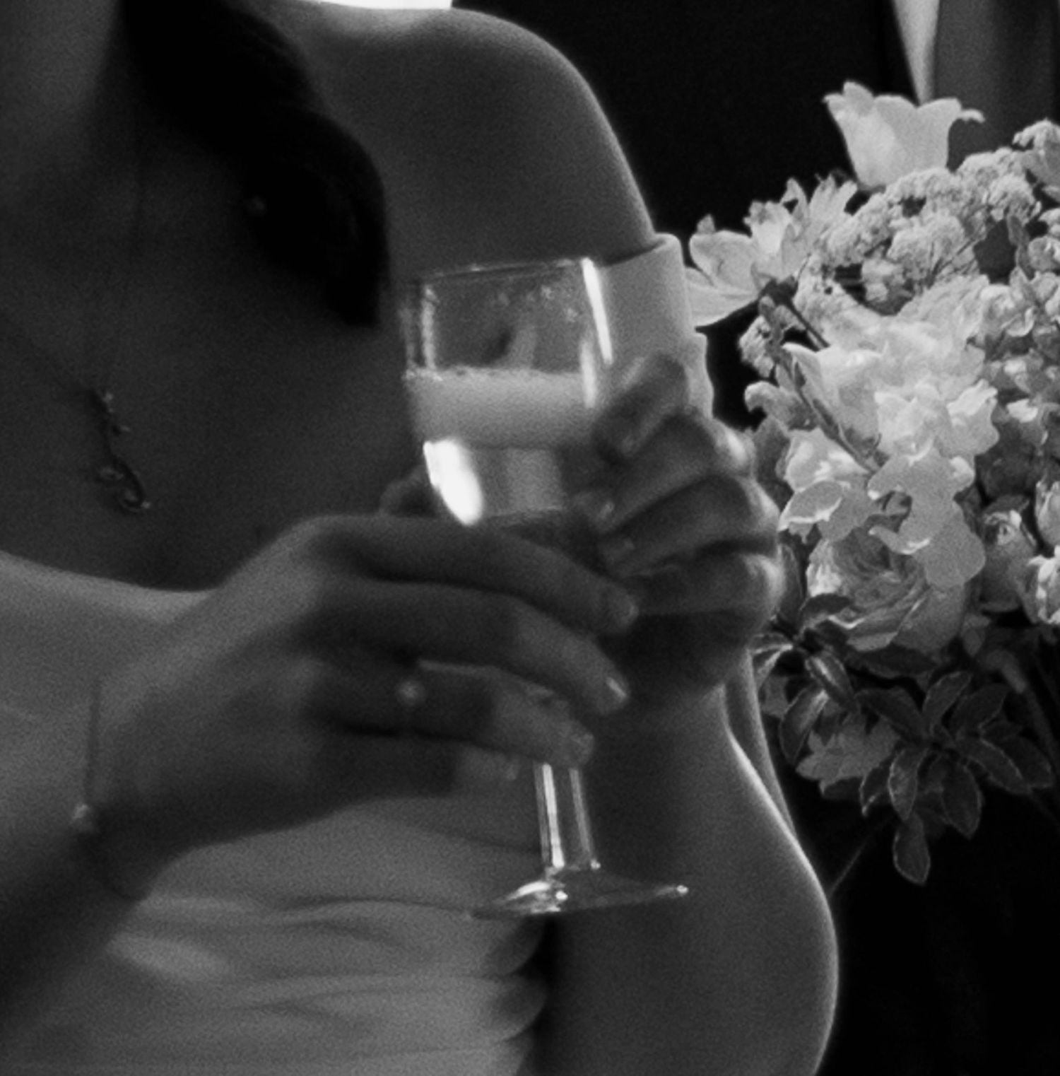 Black and white photo of a bride holding a champagne glass and wedding bouquet of white flowers.