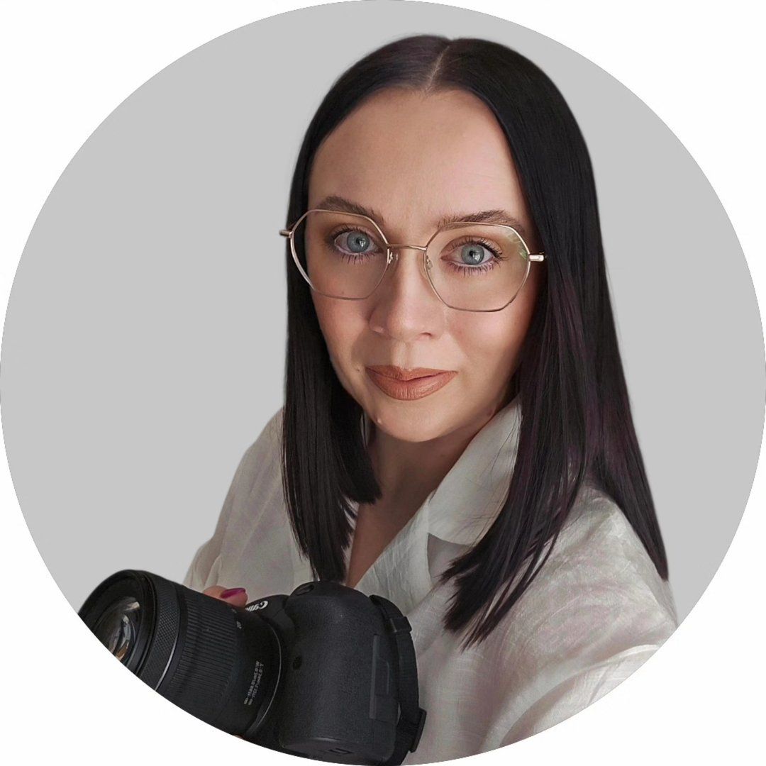 Woman with dark hair and glasses holding a professional camera, posing for a portrait photo.