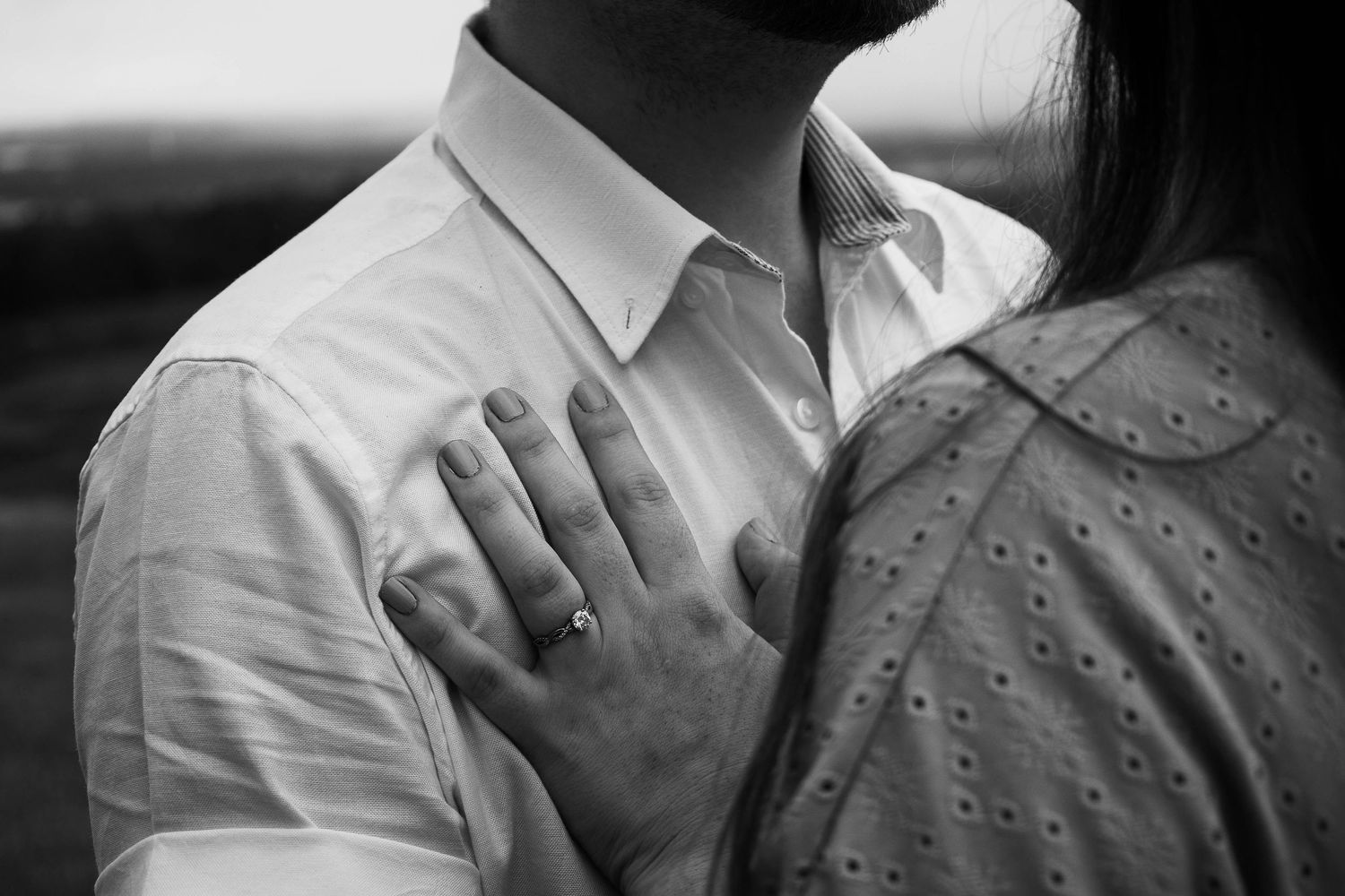 Black and white photo of a couple embracing, woman's hand with ring resting on man's white dress shirt.
