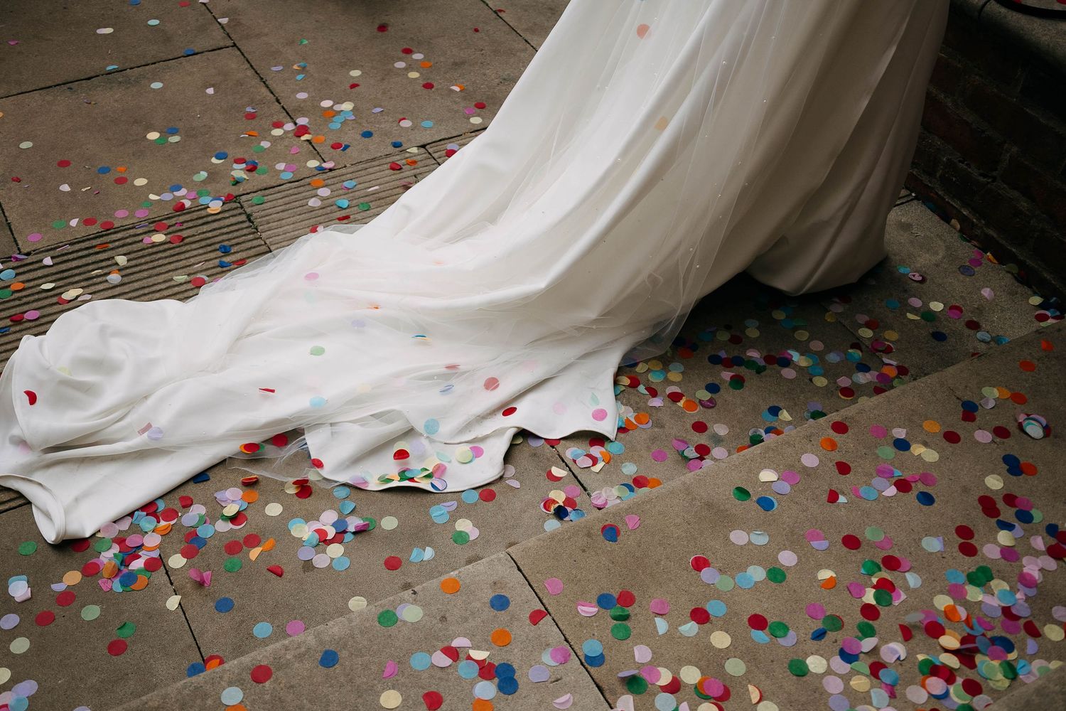White wedding dress train covered in colorful confetti circles on stone floor.