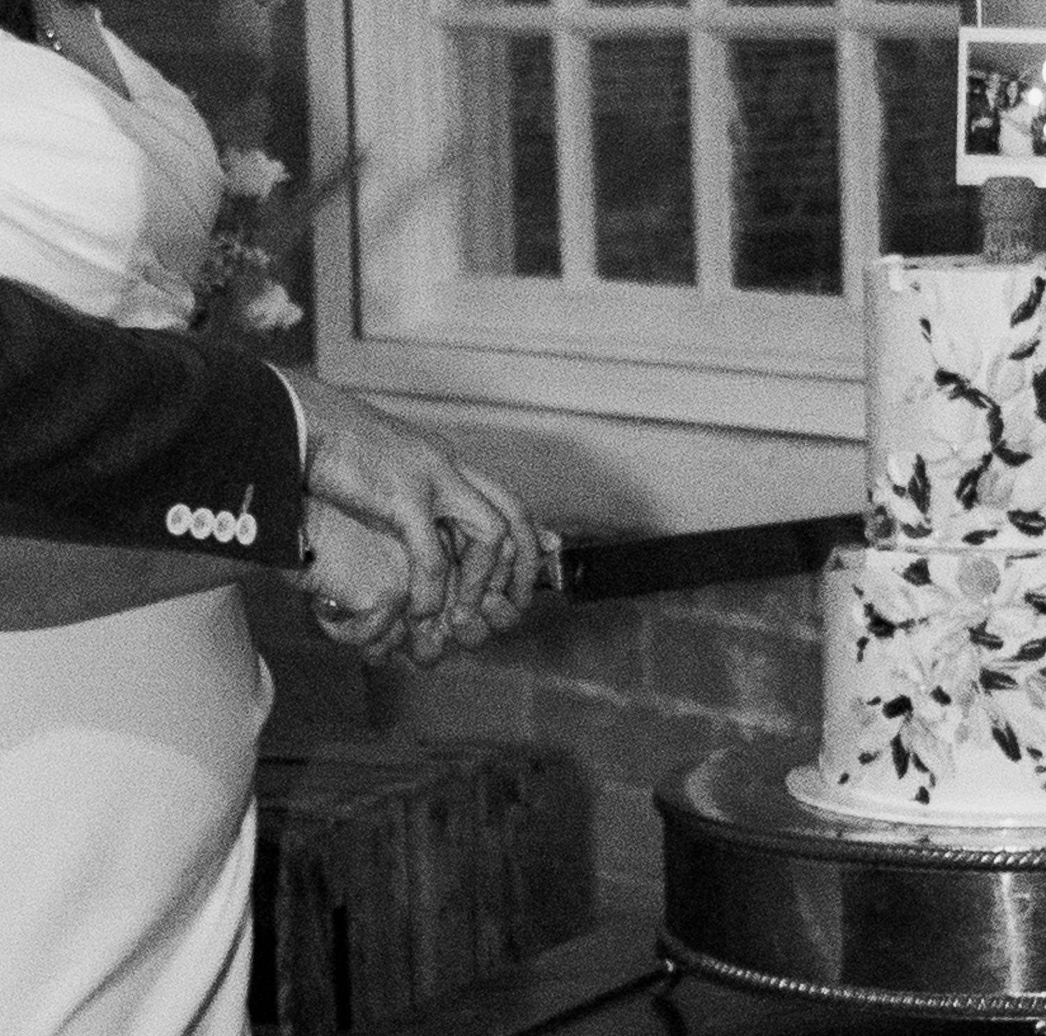 Black and white photo of a bride and groom cutting their wedding cake together at a reception.