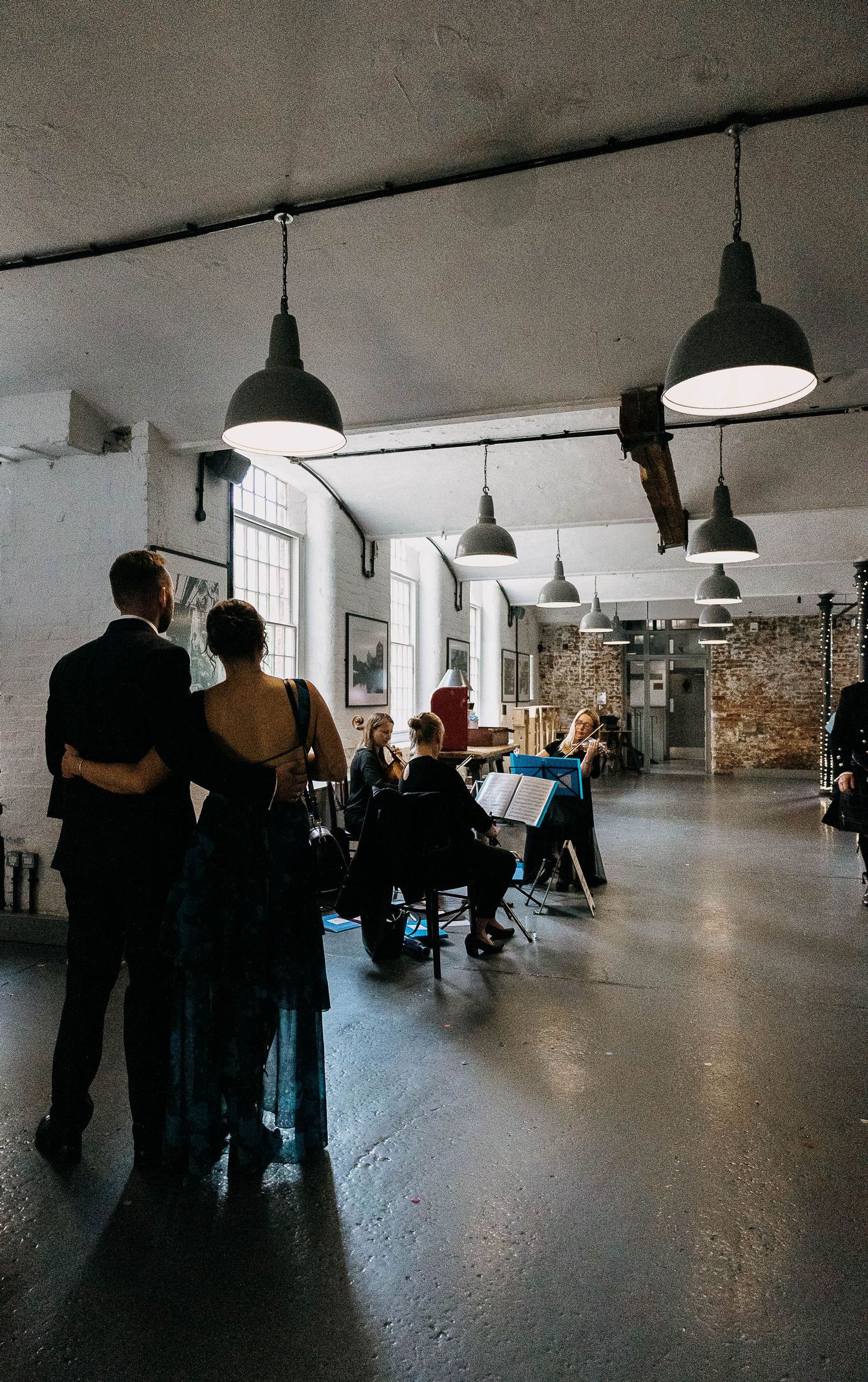Guests watch a string quartet perform in an industrial loft venue with pendant lights during a wedding reception.