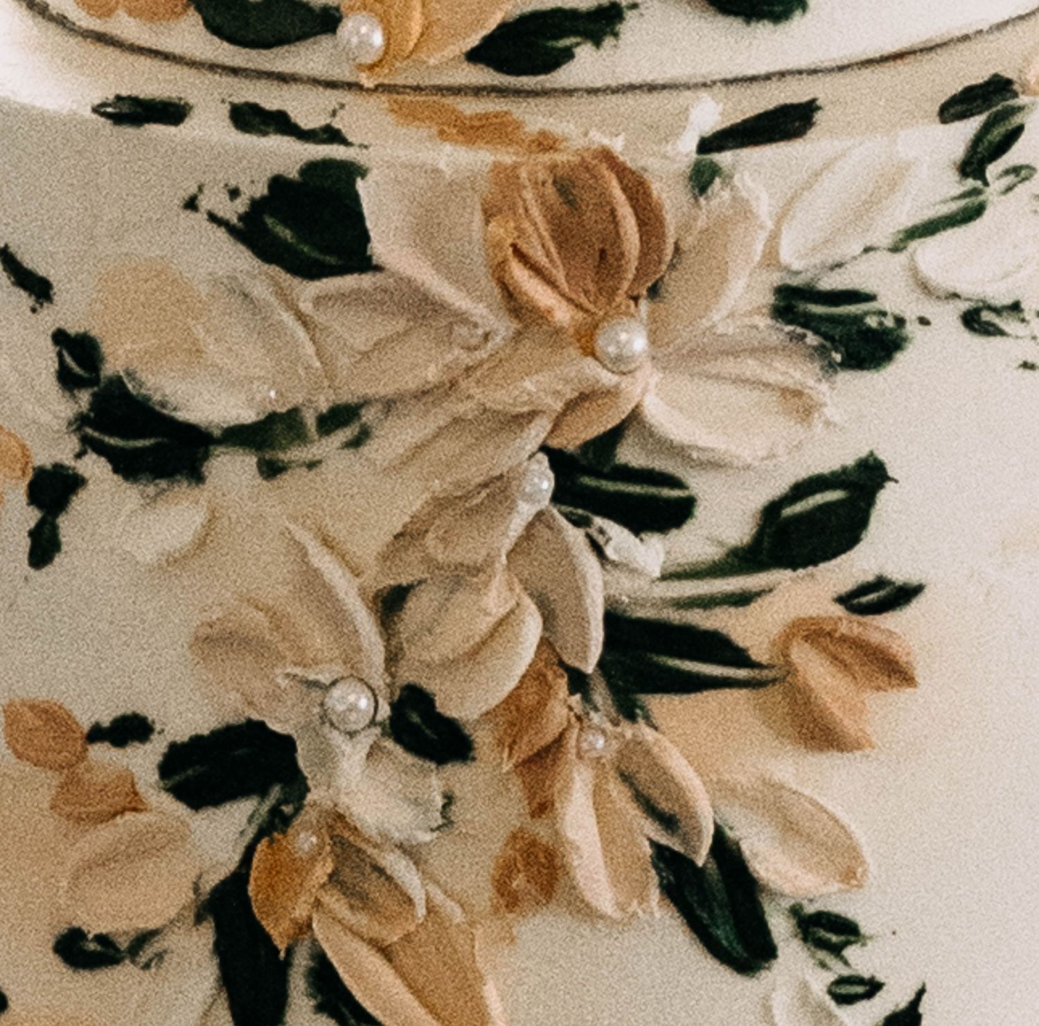 Close-up of a ceramic vase with raised floral appliques, pearl accents, and hand-painted green leaves on cream background.