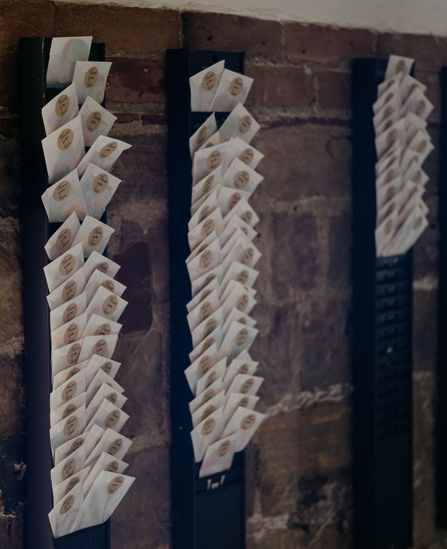 Rows of white envelopes with gold wax seals displayed on dark ribbon against a rustic brick wall.