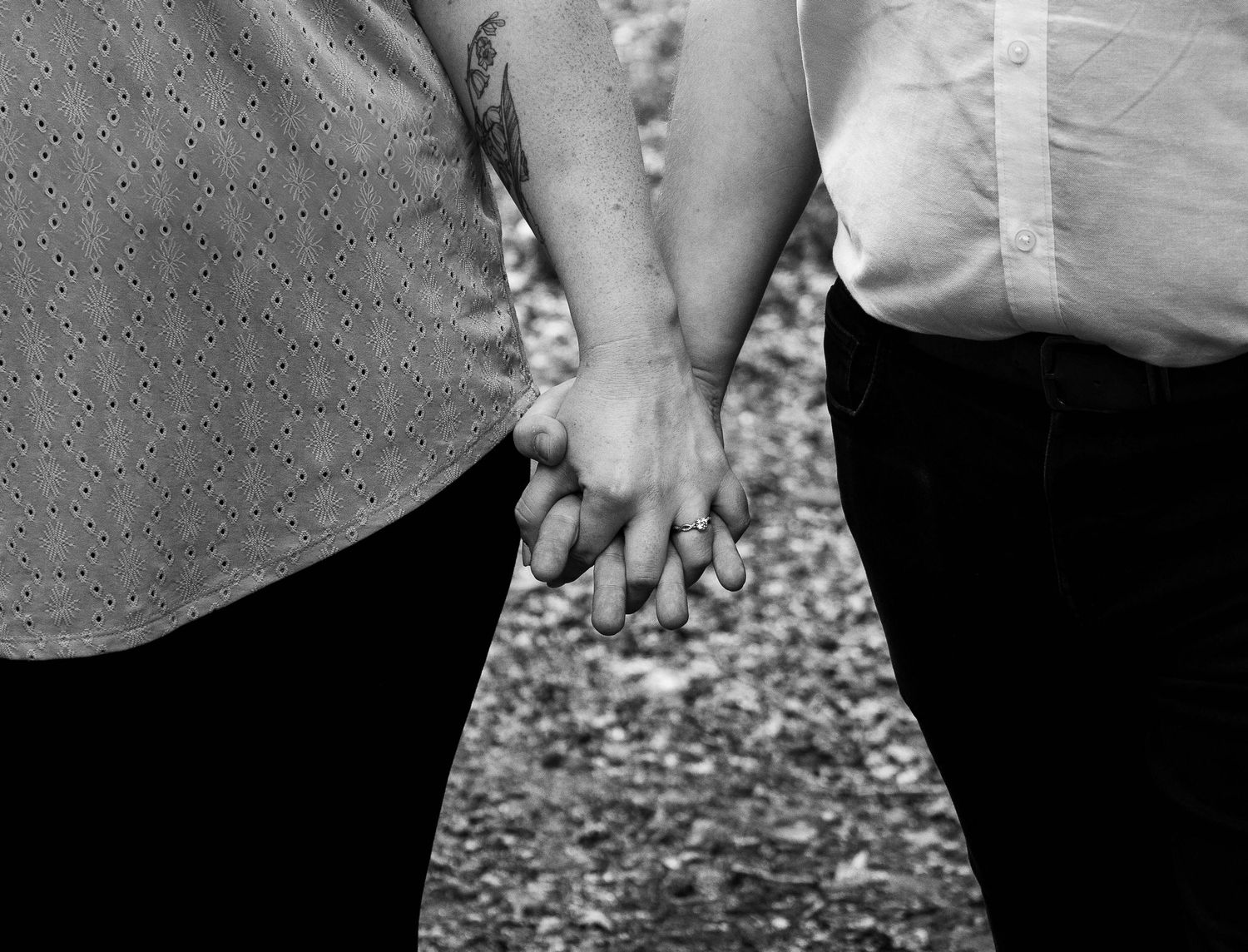Black and white photo of two people holding hands outdoors, showing a close bond and connection.