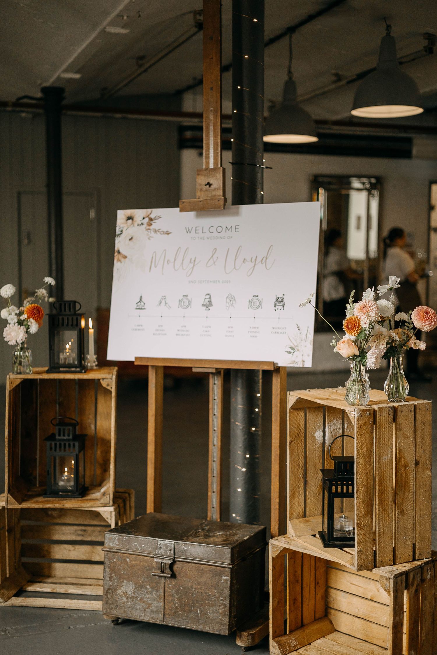 Rustic wedding welcome sign for Molly & Lloyd on wooden easel, surrounded by crates, lanterns, and floral arrangements.