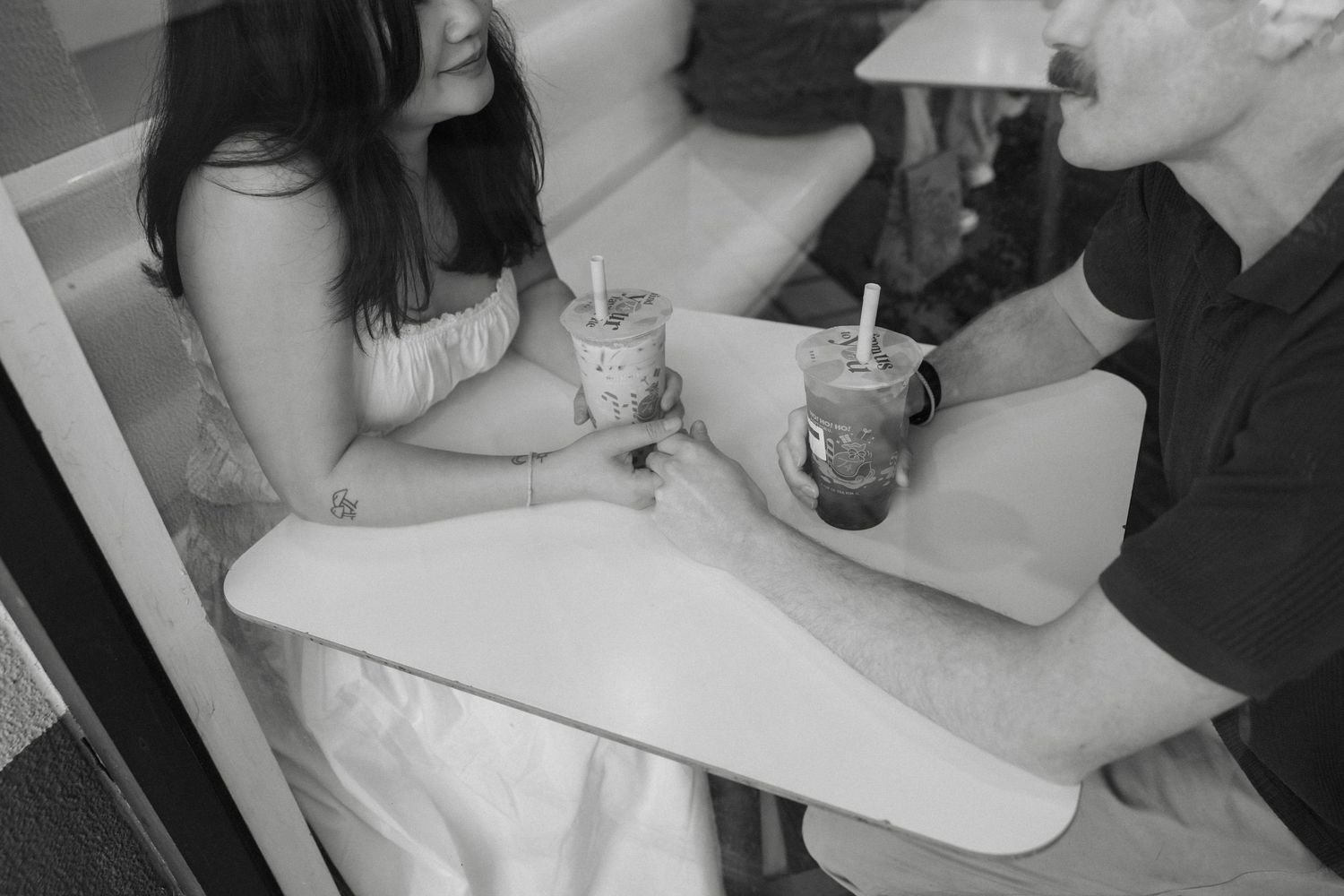 Two people sitting at a table sharing milkshakes or drinks in black and white photography.