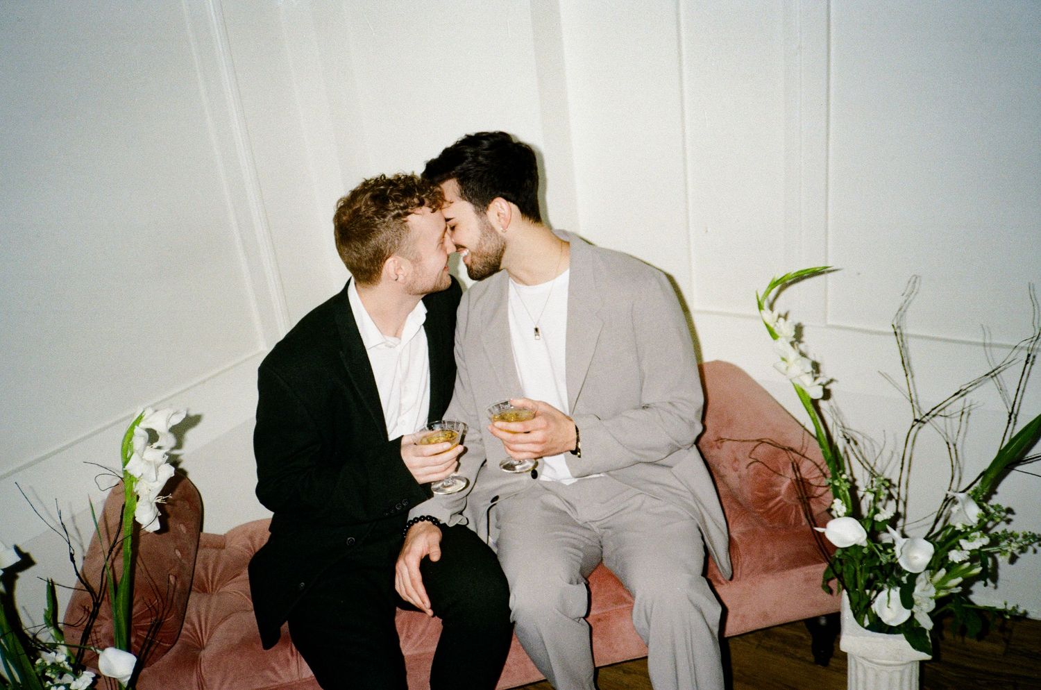 A romantic gay couple shares tender moments in a series of four intimate photographs with white floral decorations.