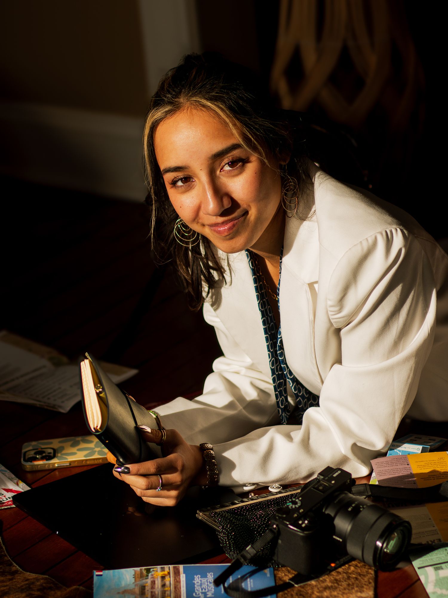 Photographer in a white coat sits at desk with camera equipment in warm lighting at night.