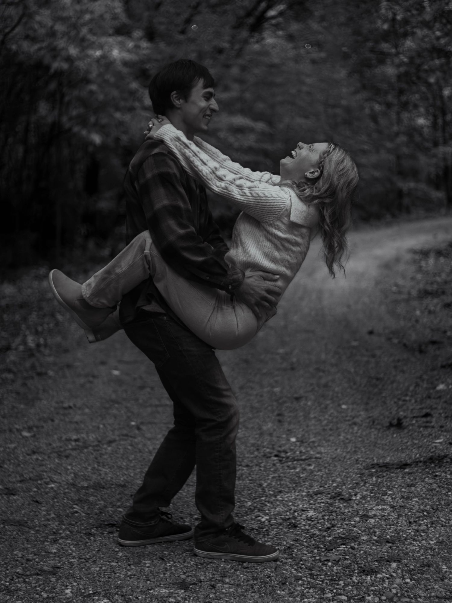 Romantic black and white photo of couple embracing on forest path.