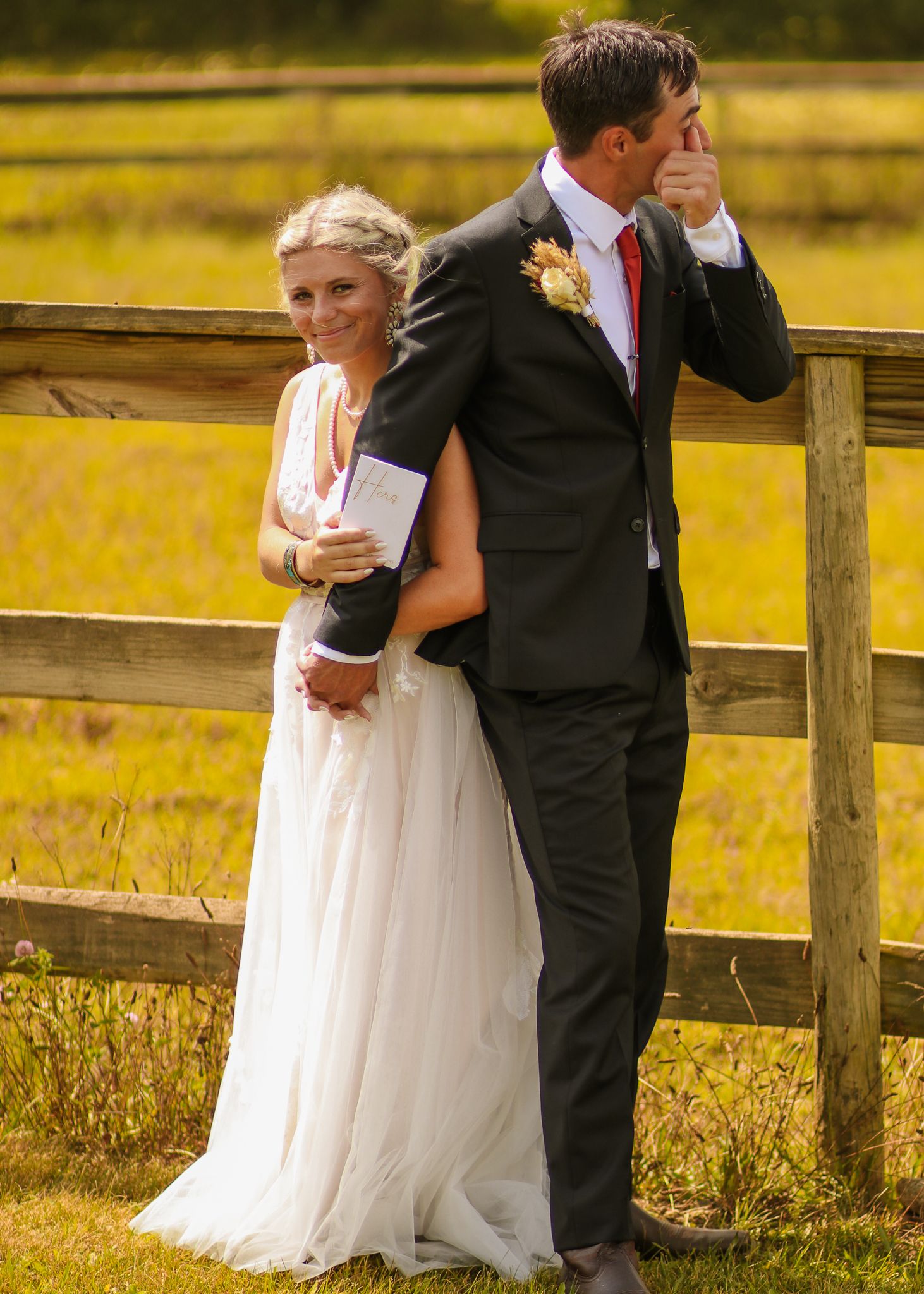 Newlyweds share an intimate moment by a rustic fence in golden sunlight.