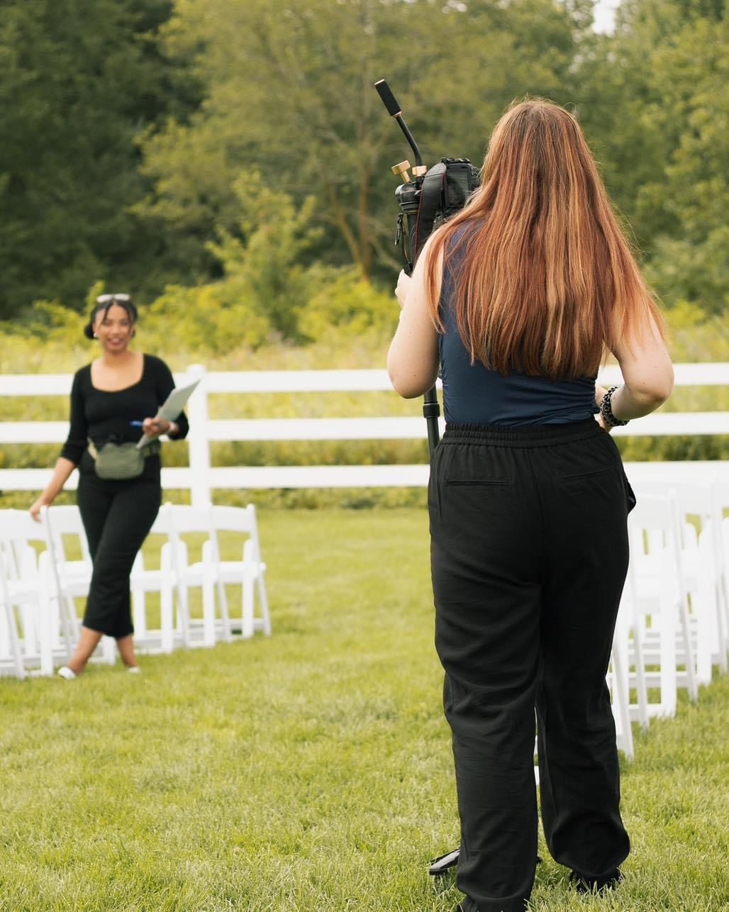 A photographer captures a scene at an outdoor wedding venue with white chairs arranged on a grass lawn.