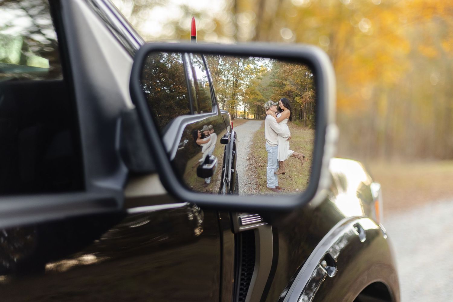 Car side mirror reflection shows two photographers with cameras working during golden autumn light in nature.