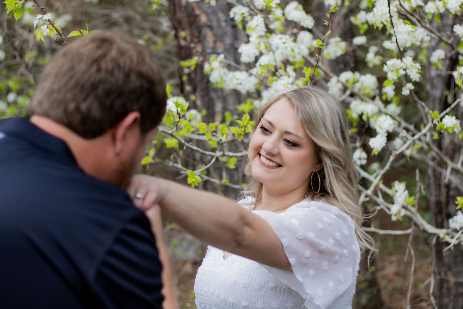 A couple embraces beneath blooming white cherry blossom trees in a romantic spring photoshoot.