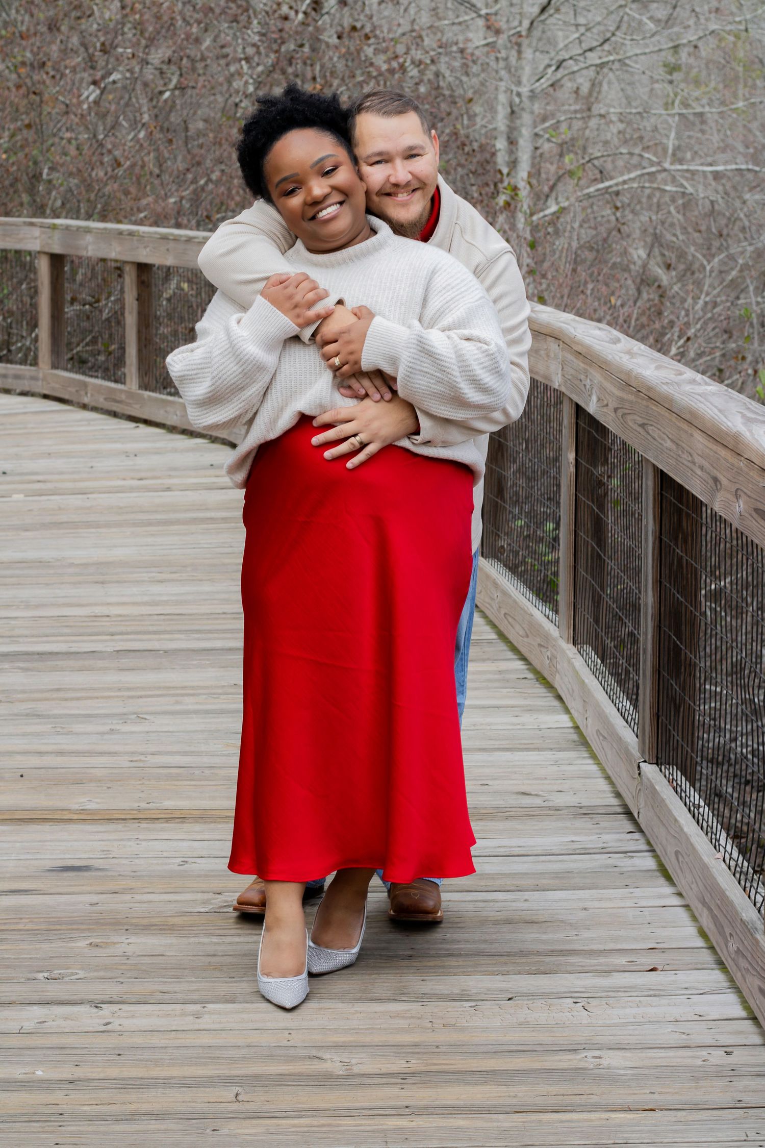 Two people sharing warm embraces on a wooden boardwalk in casual attire.