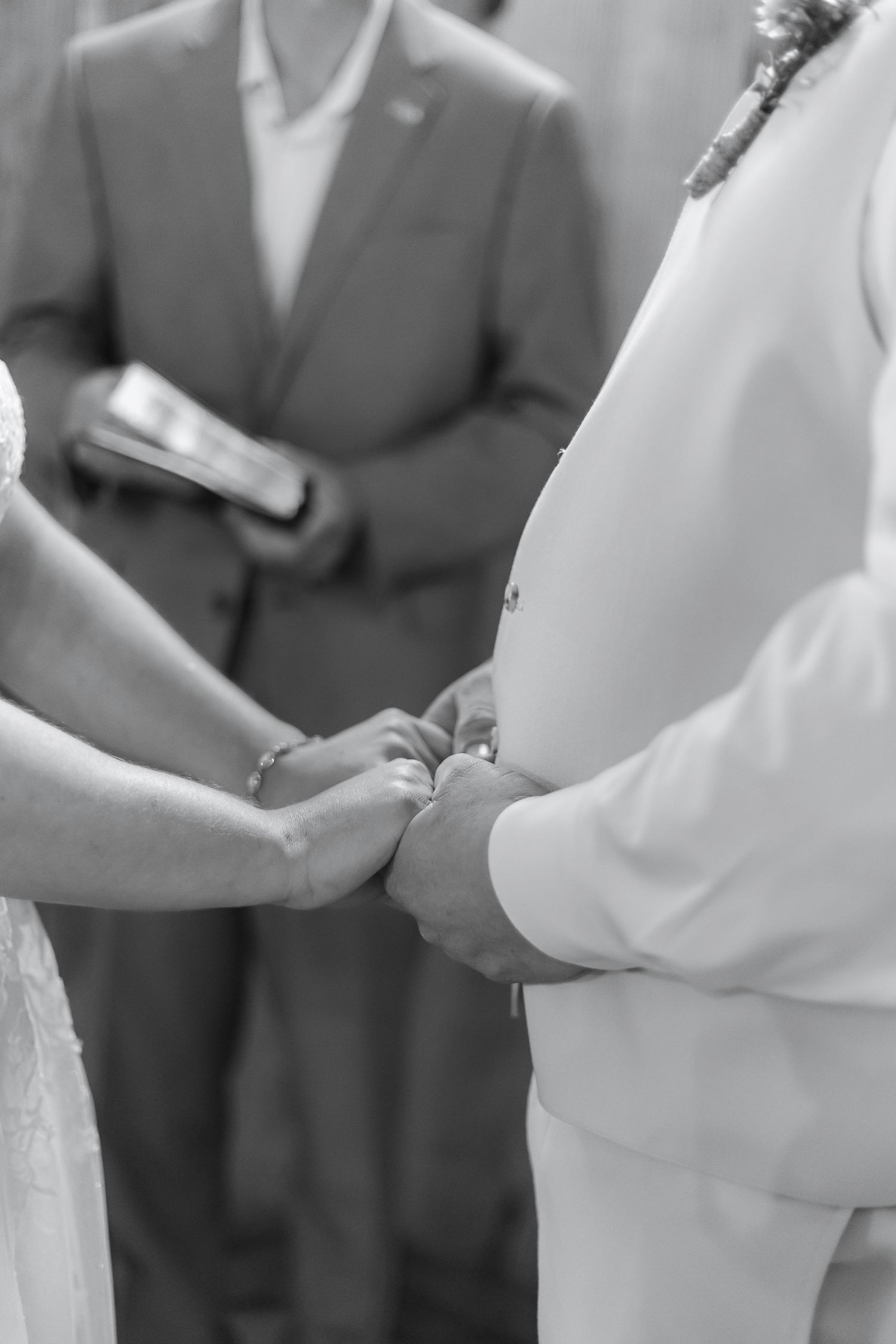 Black and white photo showing close-up of couple's hands during wedding ceremony exchange.