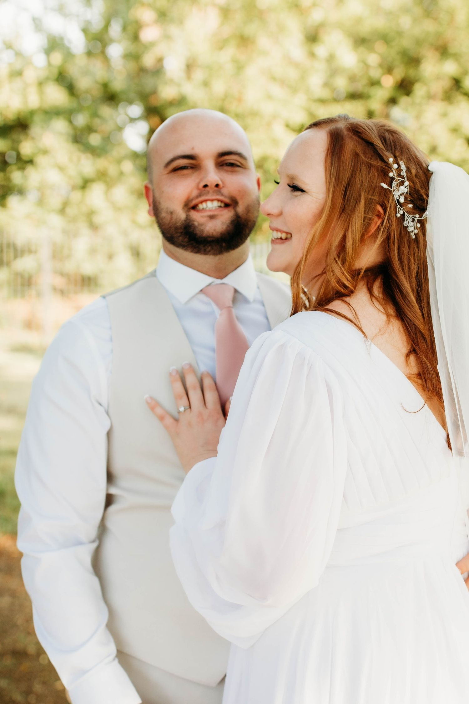 Newlywed couple in white attire sharing joyful moment outdoors during wedding photoshoot.