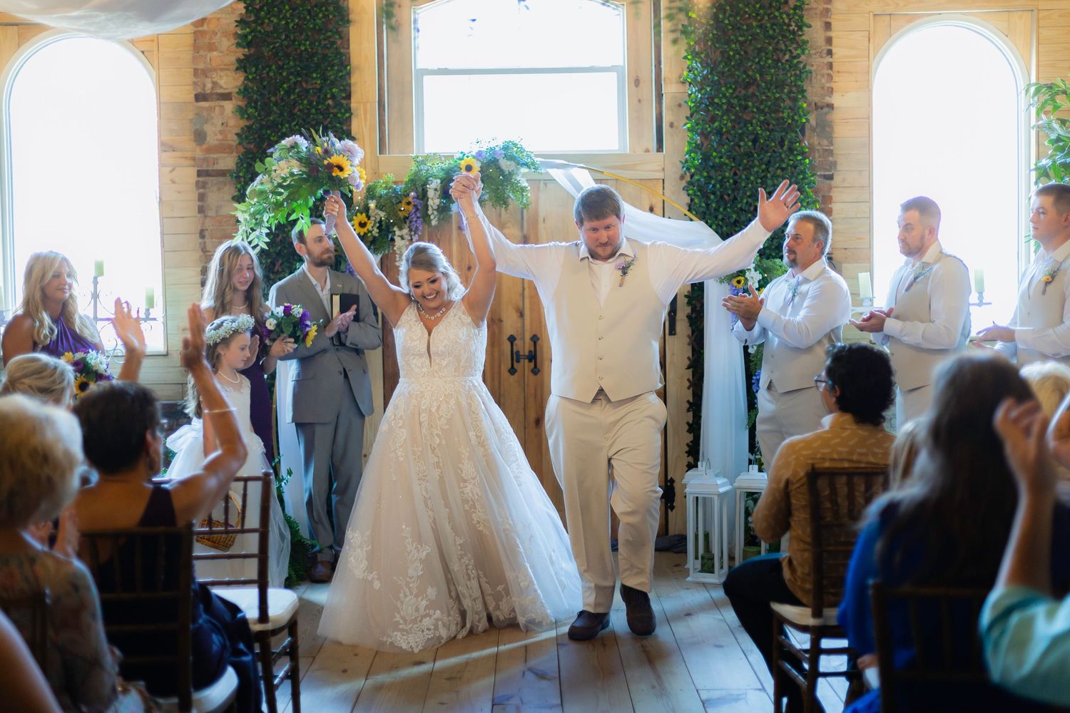 Wedding guests celebrate joyfully during an indoor reception with hands raised in the air.