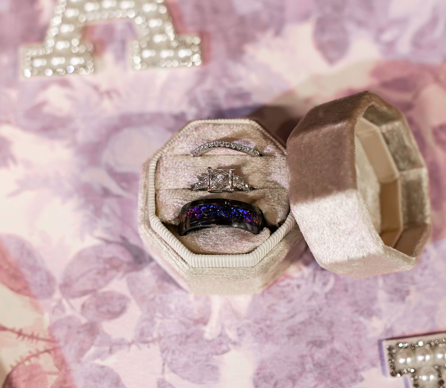 Wedding rings and jewelry photographed on pink textured background with bokeh lighting effects.