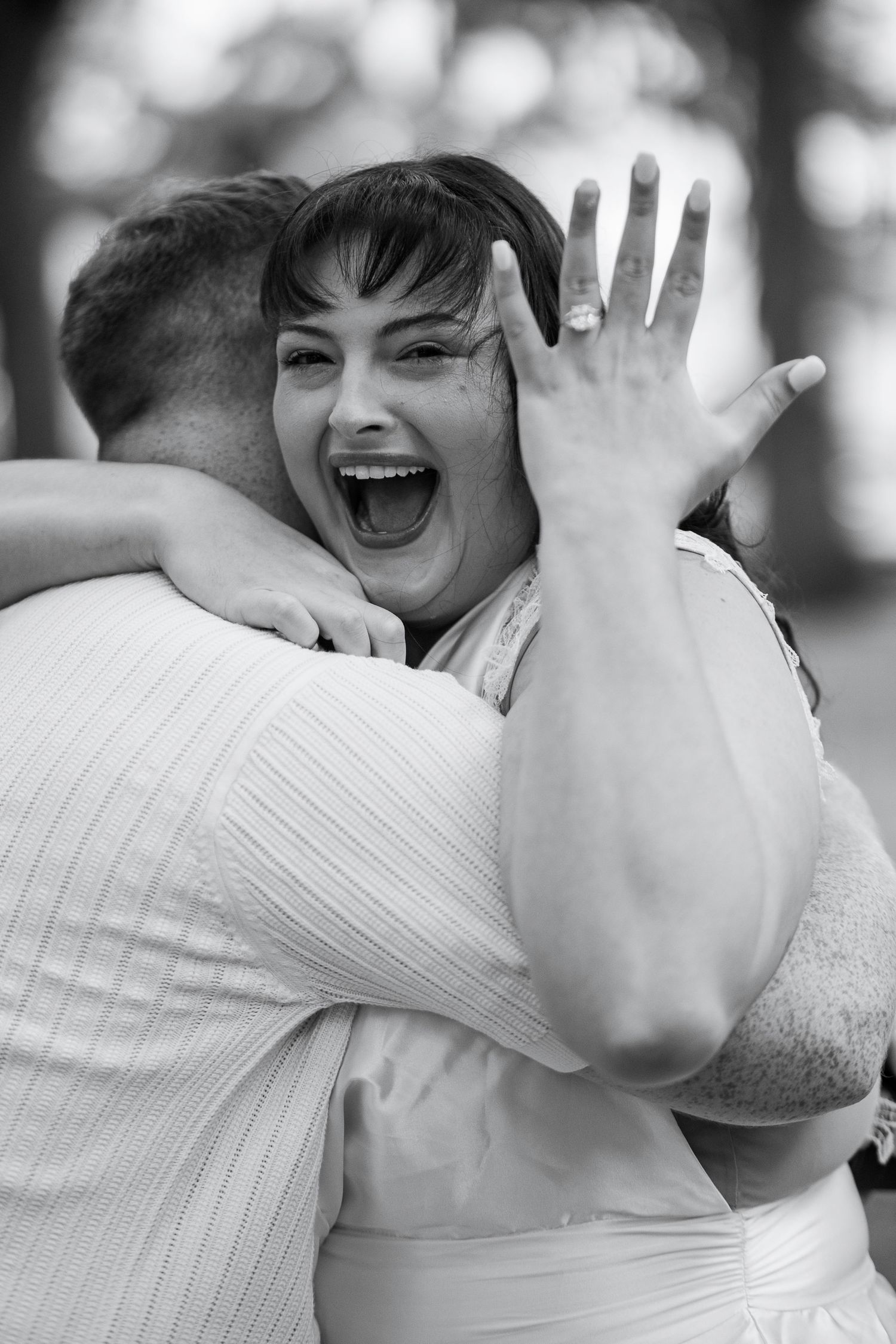 Black and white candid wedding photo showing joyful embrace between two people in white attire.