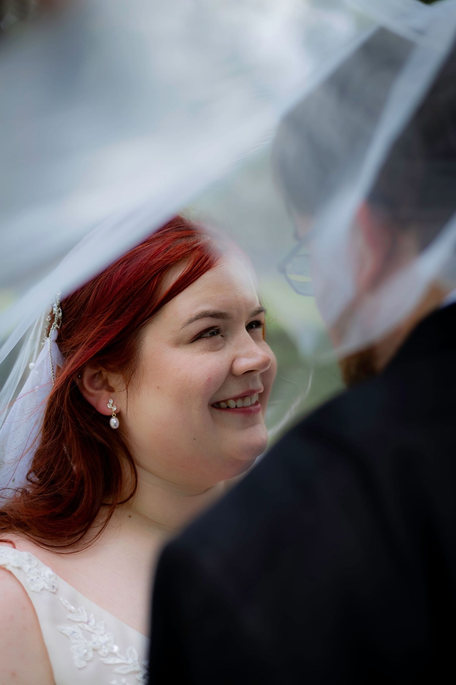 A bride in a white veil smiles warmly during her wedding day.