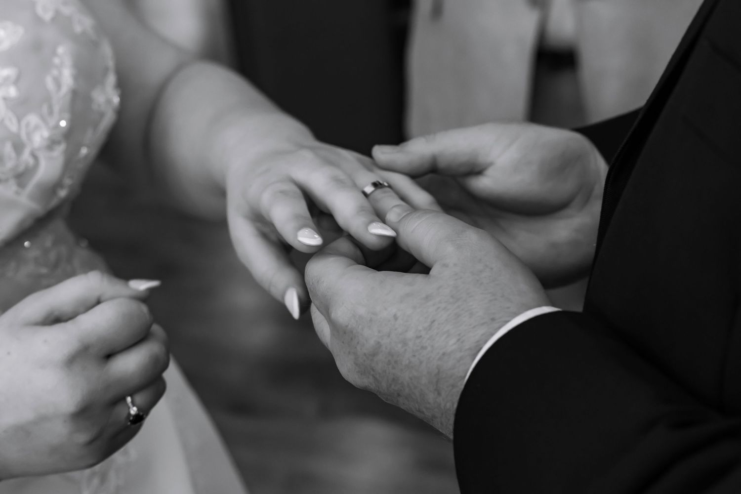 Black and white close-up of hands exchanging wedding rings during ceremony.