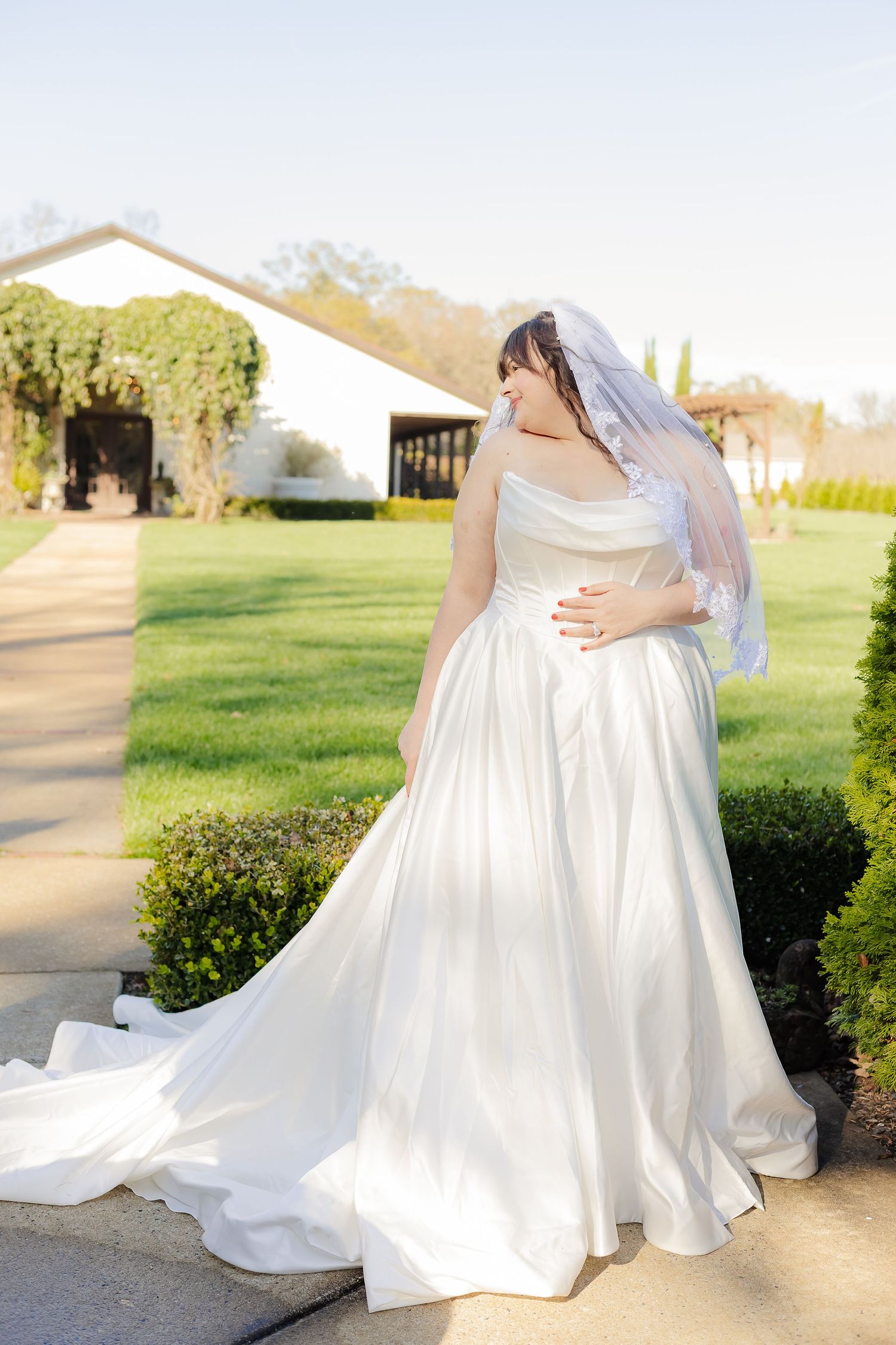 Close-up details of a flowing white wedding dress with delicate fabric draping against a sunlit outdoor background.
