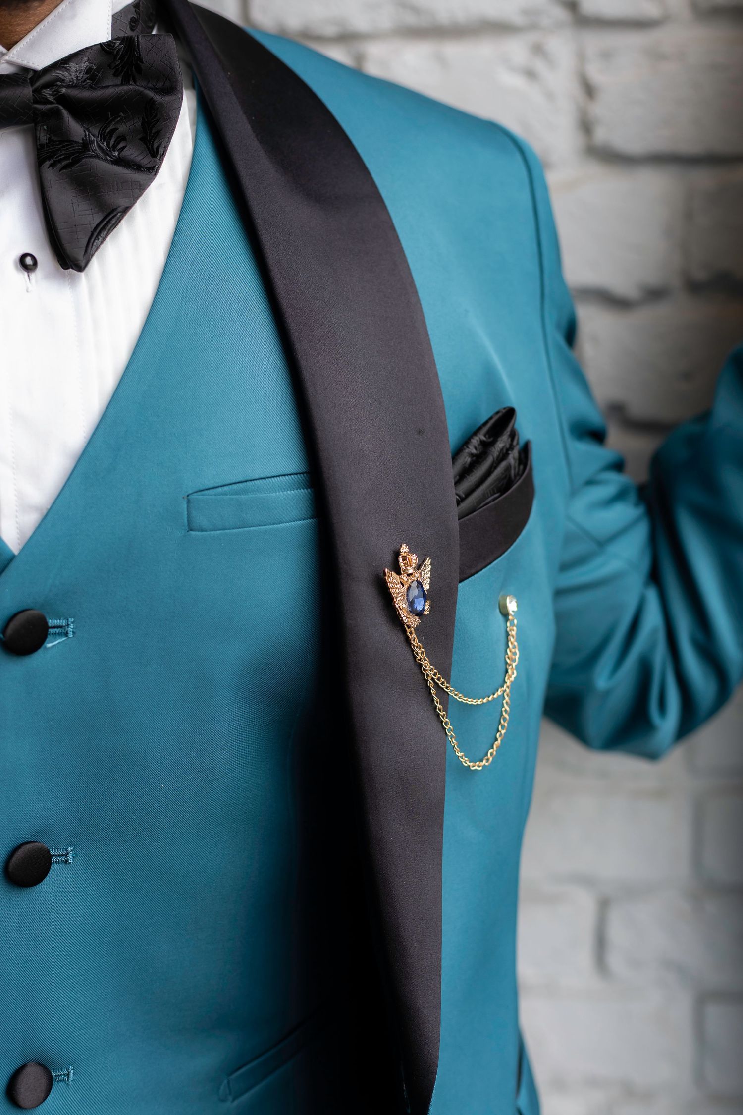 A detailed shot of a teal tuxedo jacket with black lapels and decorative chain accessory.